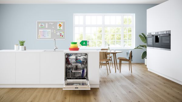 Lavastoviglie da incasso aperta in una cucina moderna con stoviglie nei cestelli e indicazione della classe energetica A